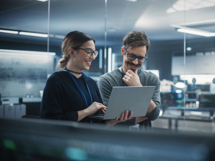 Two technologists look at a laptop together while working on an AI project in an office
